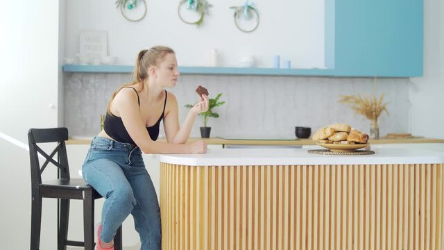 Sad bbw girl eating junk food sitting at home in the kitchen. Young fat chubby woman eating chocolate. female sitting on table doughnut, failed at sugar free low calories diet. unhealthy food