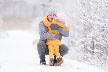 Happy young father hugging and giving love to little daughter on white snow covered trail at nature...