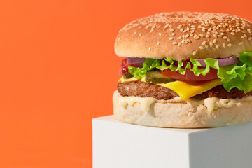 Close up fresh tasty burger on orange background. Cheeseburger with beef, tomato, pickles, lettuce and onion