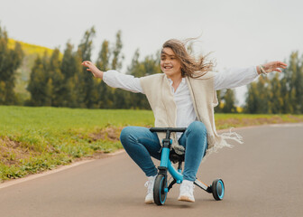 Happy female teenager riding small electric tricycle with outstretched arms on road