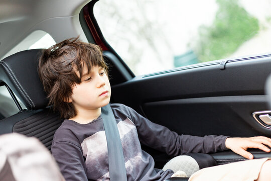 Sad pensive boy looking down is sitting in a car wearing a seat belt. Unhappy child travelling in an auto, copy space