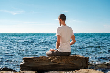 Attractive young man practicing yoga meditation and breath work outdoors by the sea
