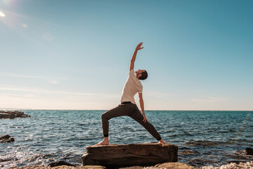 Attractive young man practicing yoga meditation and breath work outdoors by the sea
