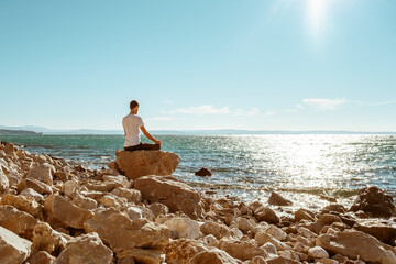 Attractive young man practicing yoga meditation and breath work outdoors by the sea
