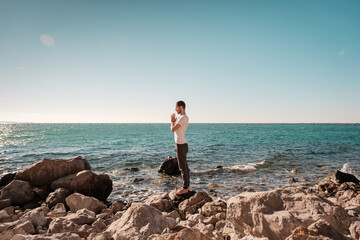 Attractive young man practicing yoga meditation and breath work outdoors by the sea
