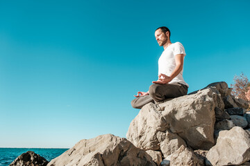 Attractive young man practicing yoga meditation and breath work outdoors by the sea
