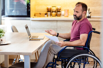 Disabled man using laptop. Mature  businessman in a wheelchair having a problem while working on wireless technology at home. Handicapped guy in wheelchair working online from home, using laptop