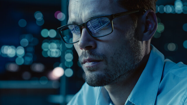 At Night Portrait Of Handsome Startup Digital Entrepreneur Working On Computer, Line Of Code Reflecting In Glasses. Developer Working On Innovative E-Commerce App Using AI Algorithm Big Data. Blue