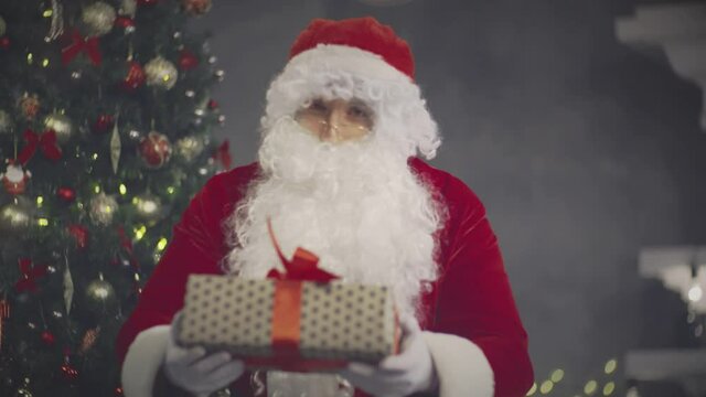 Portrait of Santa Claus with christmas gift near decorated tree. Real time