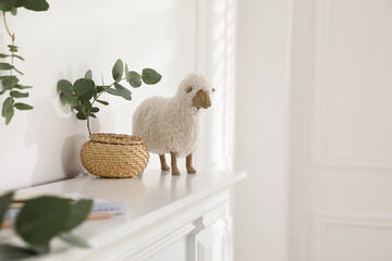 Wicker box with eucalyptus branch and decorative sheep on white shelf indoors, space for text