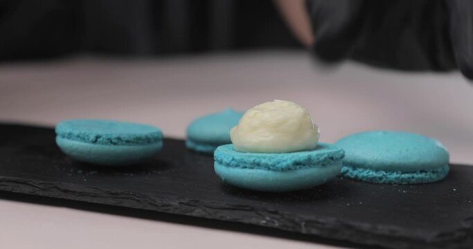 Chef with confectionery bag squeezes cream filling into macaroon shells in pastry shop. Close-up. Cooking, food and baking concept.