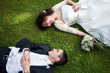 Top down view caucasian young Bride and groom lay on green grassy ground enjoy moment looking to eyes with smile. Wedding couple in love concept - 471450068