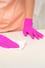 Close up of hands in rubber protective pink gloves cleaning the white surface with a white rag