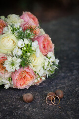 Close up golden wedding rings lay on hazelnut by bridal bouquet on grey ground surface. Flat-lay wedding photography