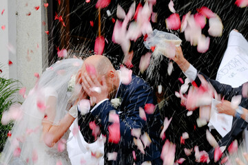 Close up wedding couple showered with rice and flower petals on wedding ceremony outside church....