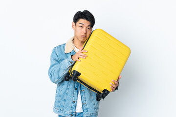 Chinese man over isolated background in vacation with travel suitcase and unhappy