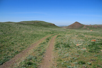 A mountain road among hills and mountains, a mountain peak in the distance, around a steppe with green grass, spurs of the Malaysary ridge, summer, sunny