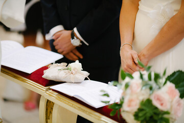 Close up wedding couple stand together by wedding rings on cushion in church at wedding ceremony