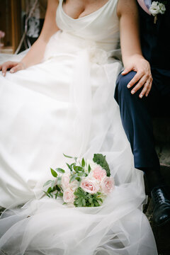 Wedding bouquet down on white bridal dress with groom and beautiful bride and groom sit close in background