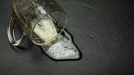 Beer is poured out of a glass mug. Spilled beer on a black table.