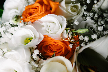 Top macro view two golden wedding rings on white orange rose bouquet flowers background with copy paste space background
