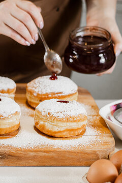 Woman chef prepares fresh donuts with jam at her bakery. Cooking traditional Hanukkah sufganiyot. Small business.