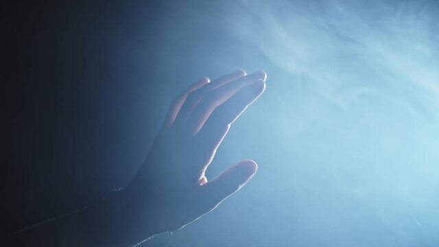 closeup of a female hand reaching to a bright light source on the right, blue