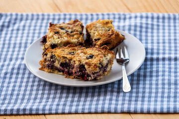 Homemade delicious sliced Apple Blueberry Pie on a white plate on a wooden table with fork and a blue cloth.