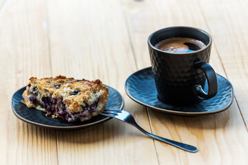 Homemade delicious sliced Apple Blueberry Pie on a black serving plate and a cup of black coffee on a wooden table. Selective Focus
