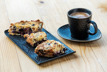 Homemade delicious sliced Apple Blueberry Pie on a black serving plate and a cup of black coffee on a wooden table. Selective Focus