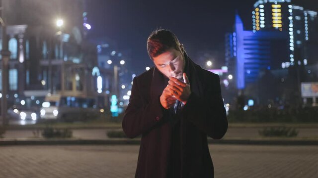 Serious attractive young man smoking cigarette at night city
