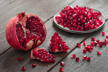ripe juicy pomegranate fruits, peeled grains in a plate and scattered on a wooden table