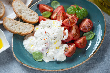 Close-up of a turquoise plate with stracciatella di bufala, cherry tomatoes and ciabatta, selective focus