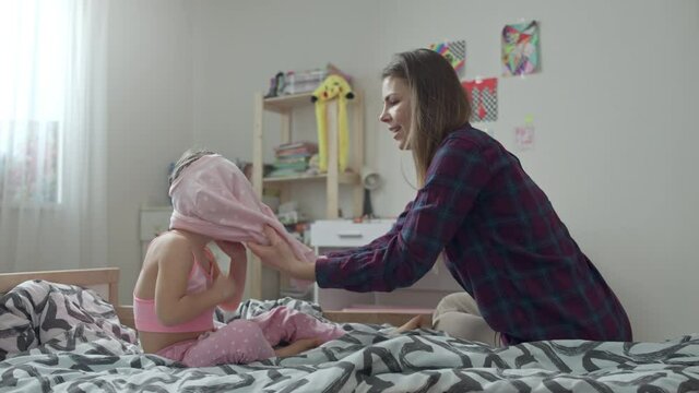 Mom puts her daughter in a sweater on the bed. Dressing a Caucasian child by a woman in the nursery.