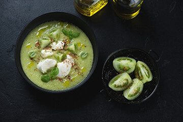 Green tomato gazpacho soup served with mozzarella, above view over black stone background, horizontal shot