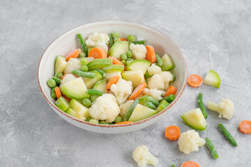 Mix of frozen vegetables in a bowl on a gray concrete background. Healthy food. Copy space.