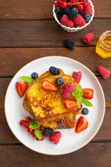 A stack of French toast on a plate with fresh berries, almond petals and honey on a dark wooden background. Delicious breakfast. Copy space.