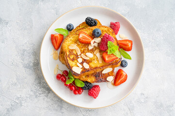 A stack of French toast on a plate with fresh berries, almond petals and honey on a gray concrete...