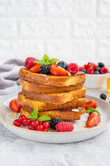 A stack of French toast on a plate with fresh berries, almond petals and honey on a gray concrete background. Delicious breakfast. Copy space.