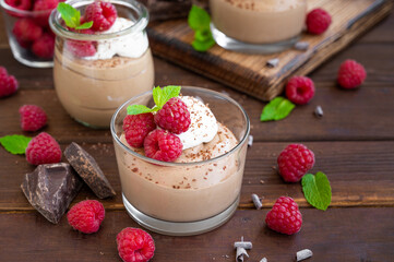 Chocolate mousse with whipped cream and fresh raspberries in a glass on a dark wooden background. Copy space.