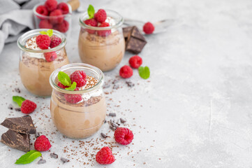 Chocolate mousse with whipped cream and fresh raspberries in a glass on a gray concrete background. Copy space.