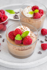 Chocolate mousse with whipped cream and fresh raspberries in a glass on a gray concrete background. Copy space.