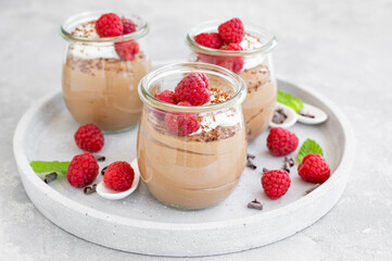 Chocolate mousse with whipped cream and fresh raspberries in a glass on a gray concrete background. Copy space.