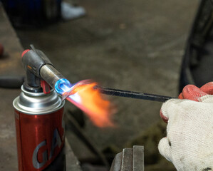 Naklejka premium Photo of a gas burner and metal melting. Male hands in work gloves in the garage