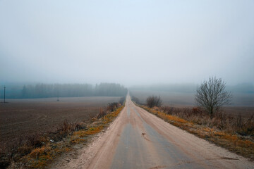 Autumn road through foggy landscape. Autumn foggy rustic landscape with asphalt road in background....