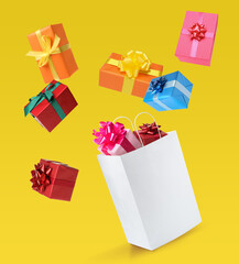 Many different gift boxes falling into paper shopping bag on yellow background
