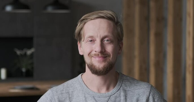 Closeup portrait of smiling European blonde guy posing at luxury apartment loft interior. Face of confident casual successful business male freelancer employee self employment boss or modern happy man