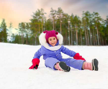 childhood, leisure and season concept - happy little girl in winter clothes outdoors over snowy forest or park background