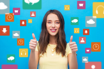 media and people concept - smiling young woman or teenage girl in blank yellow t-shirt showing thumbs up over virtual icons on bright blue background