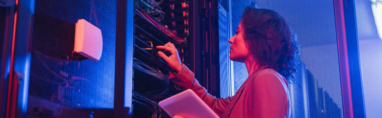 engineer holding digital tablet while checking server in data center in neon light, banner